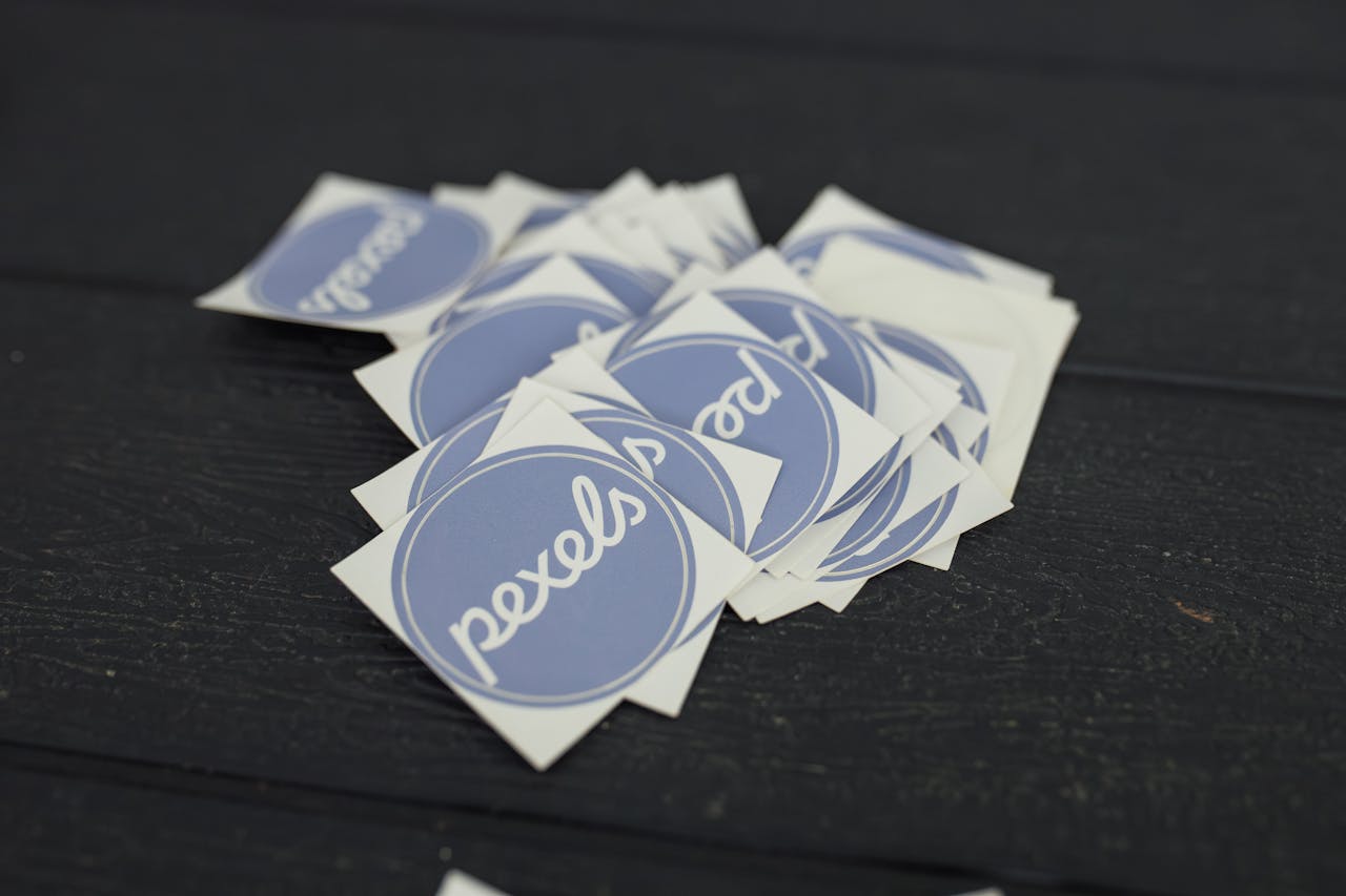 services-02 A pile of Pexels logo stickers arranged on a dark wooden surface.
